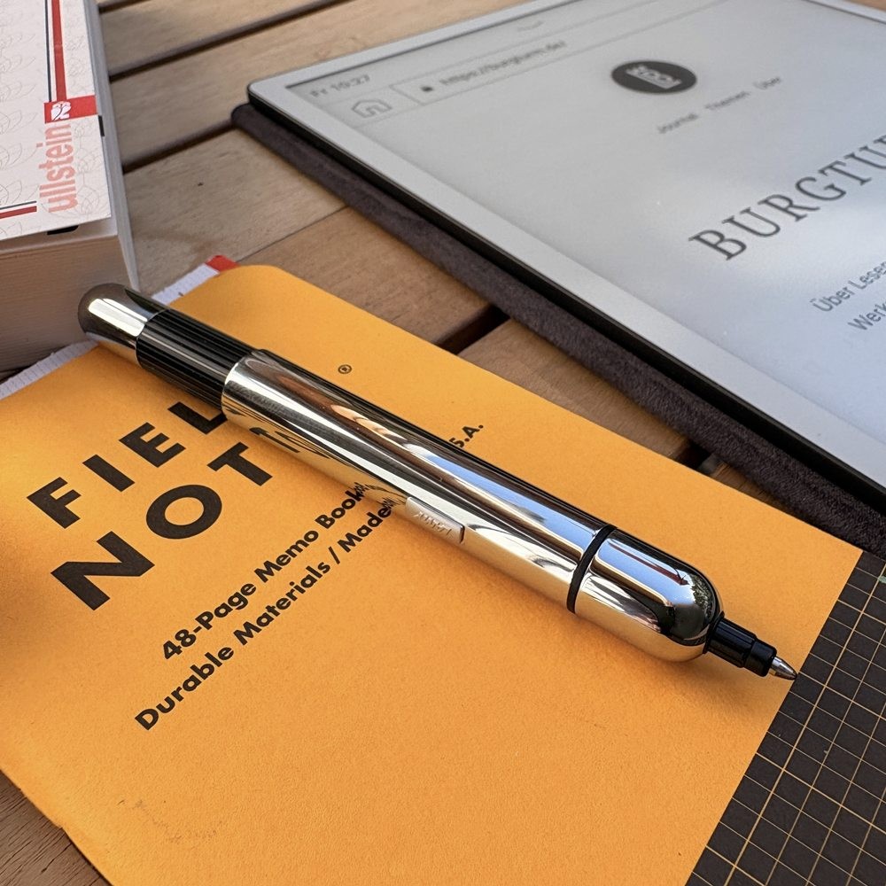 Ausgefahrener LAMY pico chrome auf einem gelben Field Notes Notizbuch neben einem E-Ink-Reader