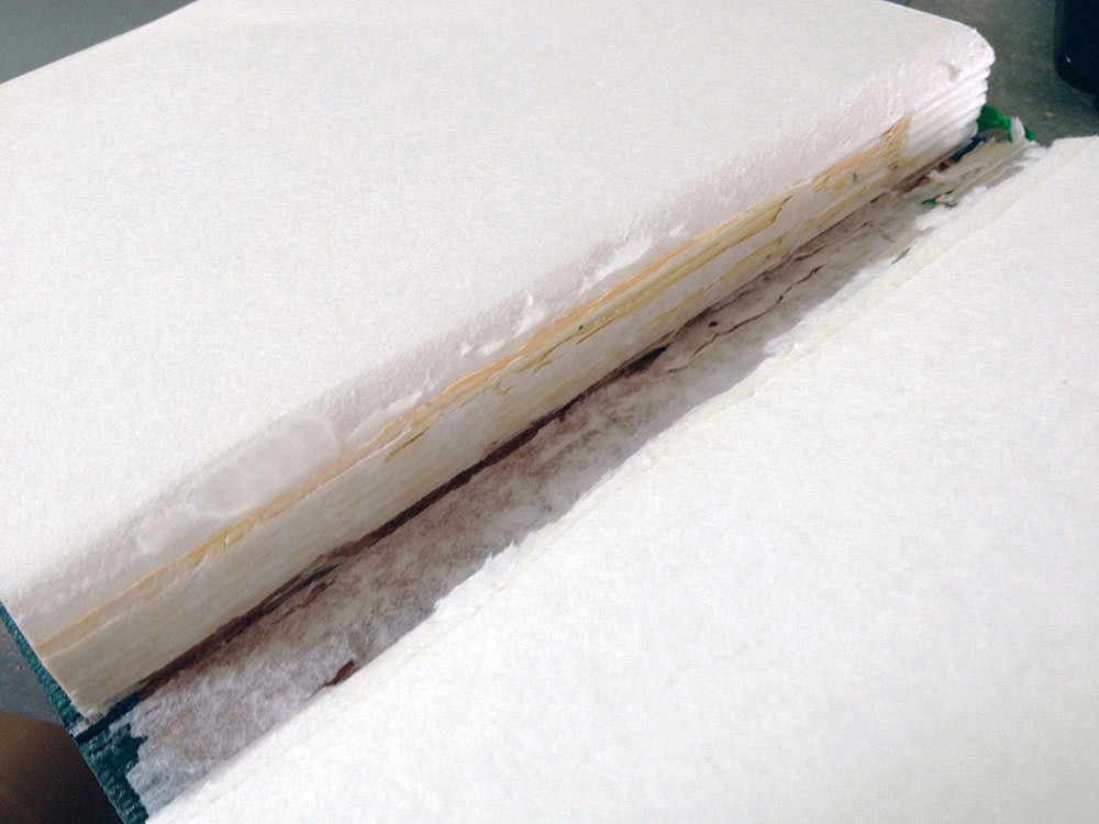 Geöffneter Buchrücken eines Notizbuchs mit sichtbarem Leim und schlechter Verklebung.