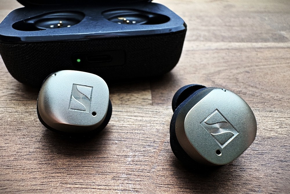 Sennheiser MOMENTUM True Wireless 4 vor geöffneten Ladecase auf einem Schreibtisch