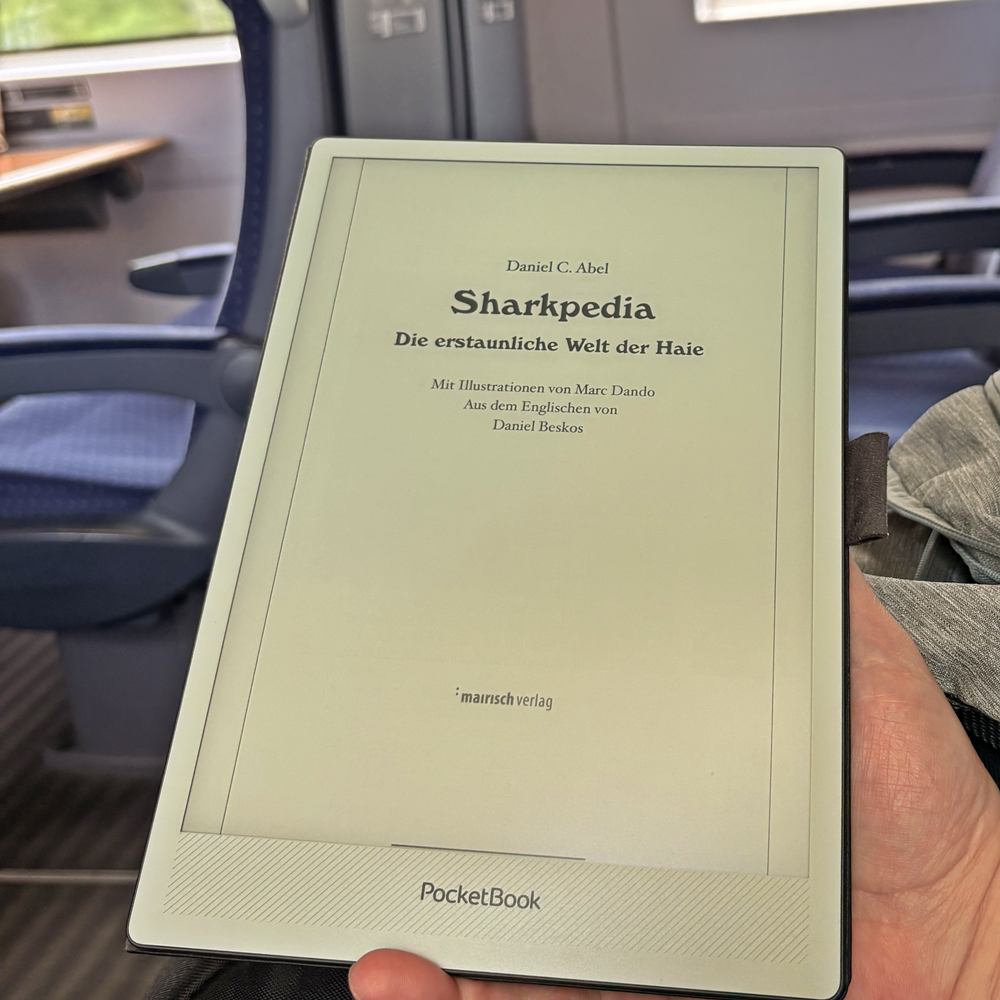 PocketBook InkPad One mit dem geöffneten E-Book „Sharkpedia“ in einem Zugabteil