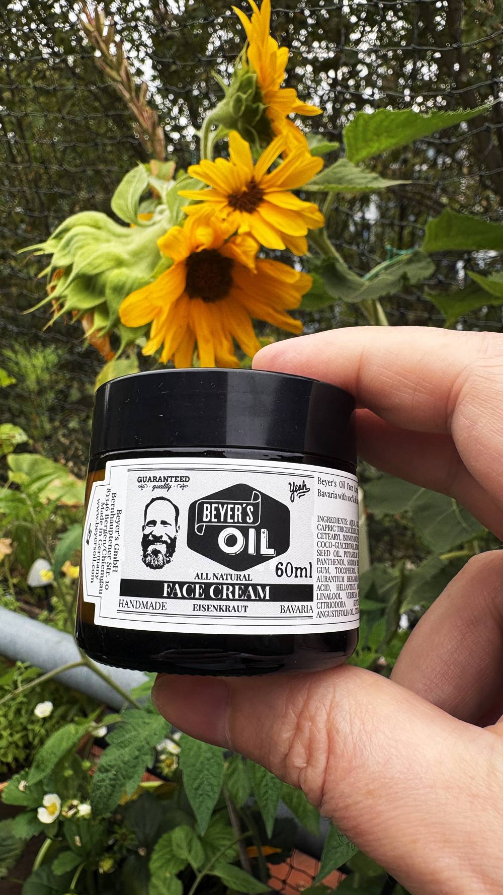 Beyer’s Oil Gesichtscreme Eisenkraut in der Hand vor Sonnenblumen