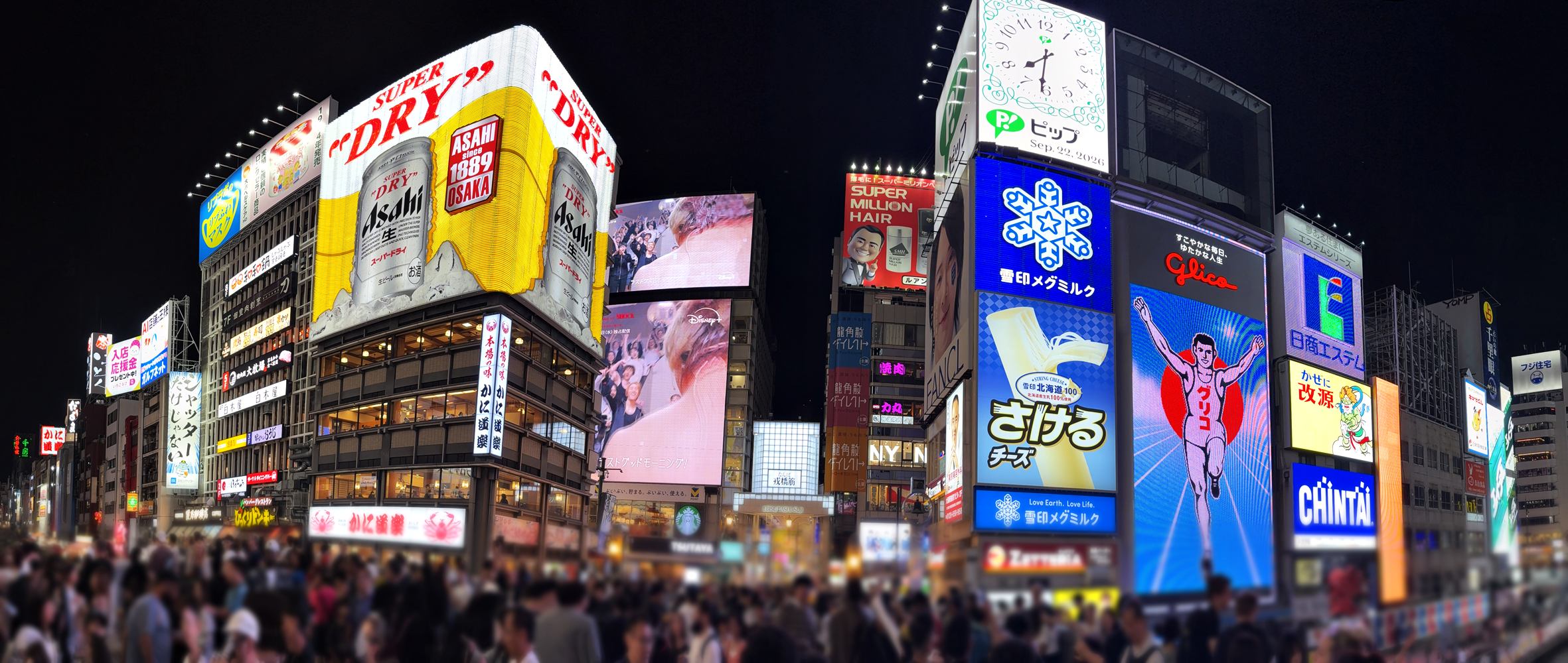 Nächtliches Panorama von Dōtonbori in Osaka mit bunten Leuchtreklamen, vielen Menschen und dem Kanal.